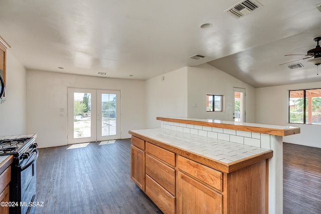 kitchen featuring gas range, dark hardwood / wood-style floors, ceiling fan, a kitchen island, and tile counters