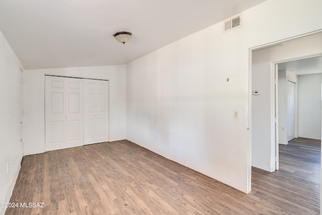 unfurnished bedroom with lofted ceiling, hardwood / wood-style flooring, and a closet