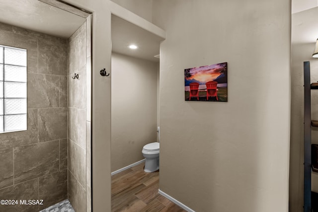 bathroom with hardwood / wood-style floors, toilet, a tile shower, and a healthy amount of sunlight