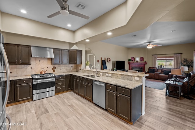 kitchen featuring stainless steel appliances, kitchen peninsula, sink, ceiling fan, and wall chimney exhaust hood