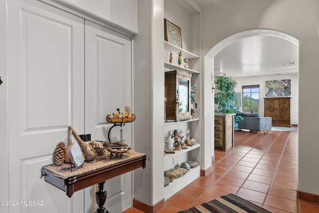 hallway featuring built in shelves, arched walkways, tile patterned floors, and baseboards