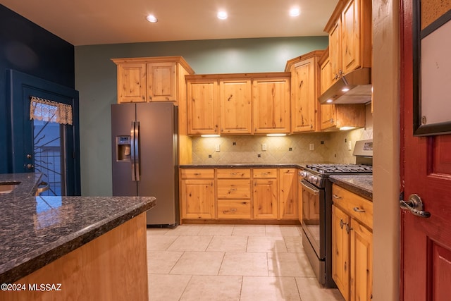 kitchen with dark stone counters, black gas range oven, decorative backsplash, light tile patterned floors, and stainless steel fridge