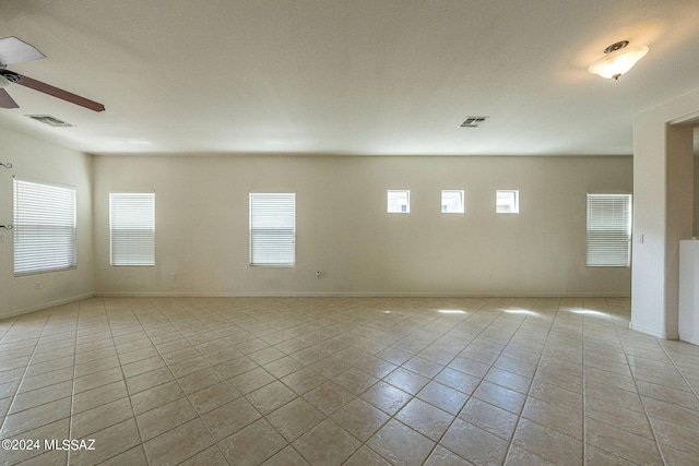 empty room with ceiling fan, light tile patterned flooring, visible vents, and baseboards