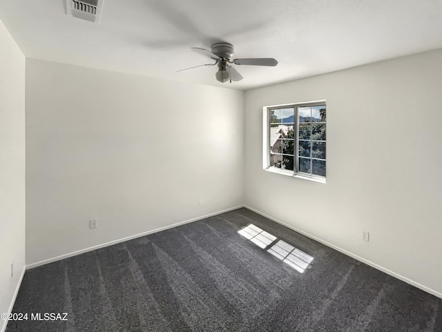 empty room featuring dark colored carpet, visible vents, ceiling fan, and baseboards