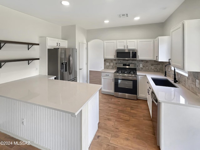 kitchen featuring white cabinets, appliances with stainless steel finishes, a peninsula, light countertops, and a sink