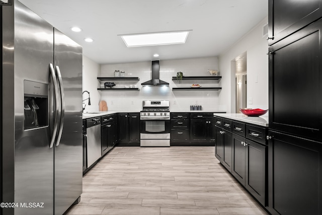 kitchen with decorative backsplash, appliances with stainless steel finishes, light hardwood / wood-style flooring, wall chimney exhaust hood, and sink