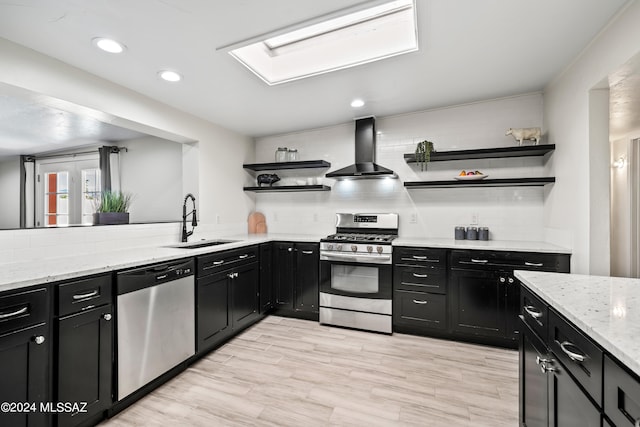 kitchen featuring wall chimney range hood, sink, light wood-type flooring, appliances with stainless steel finishes, and tasteful backsplash