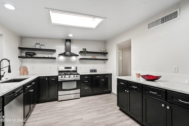 kitchen featuring decorative backsplash, light wood-type flooring, sink, wall chimney exhaust hood, and stainless steel appliances