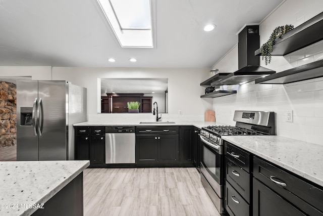 kitchen with appliances with stainless steel finishes, sink, a skylight, light stone countertops, and light hardwood / wood-style flooring