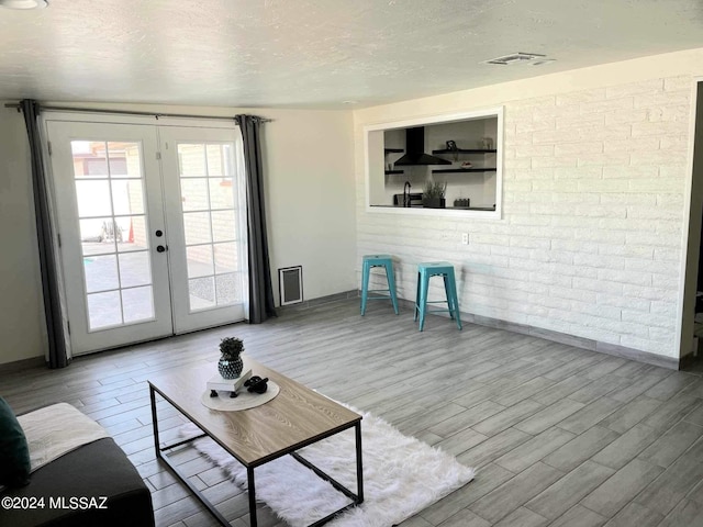 unfurnished living room featuring french doors, brick wall, wood-type flooring, and a textured ceiling