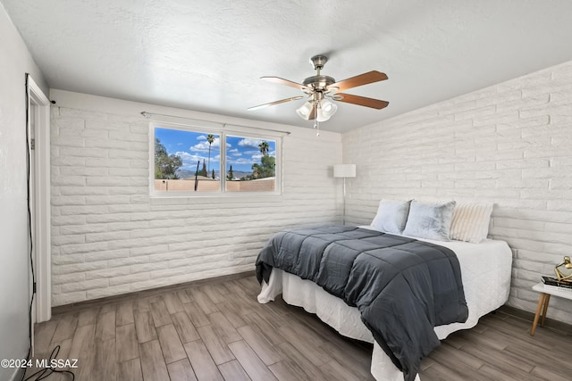 bedroom featuring hardwood / wood-style floors, a textured ceiling, brick wall, and ceiling fan