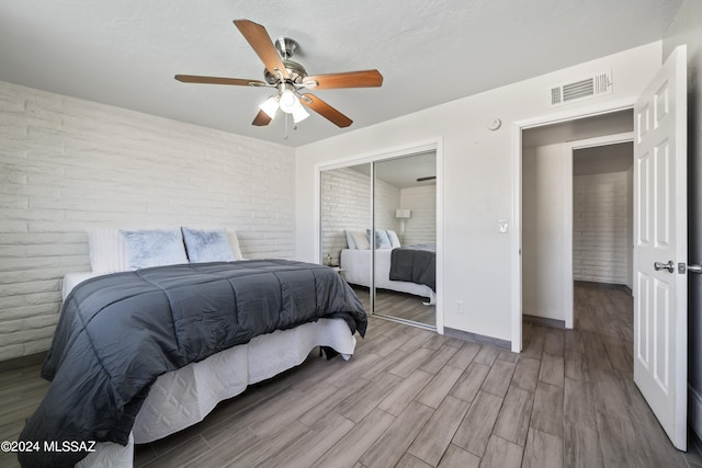 bedroom featuring brick wall, light hardwood / wood-style flooring, a closet, and ceiling fan