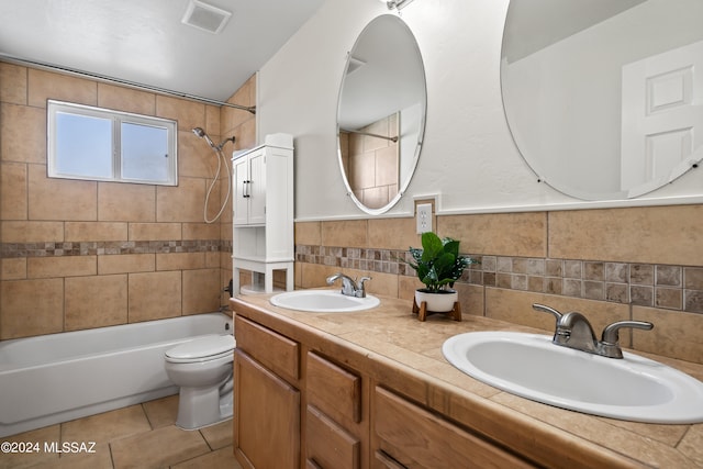 full bathroom with toilet, tile patterned flooring, vanity, tiled shower / bath combo, and tile walls