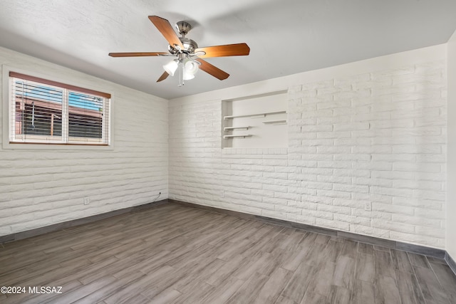 empty room featuring ceiling fan, hardwood / wood-style flooring, and brick wall