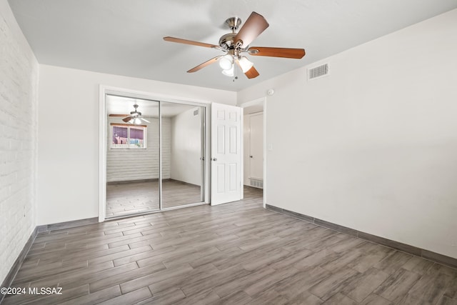 unfurnished bedroom with a closet, hardwood / wood-style flooring, brick wall, and ceiling fan