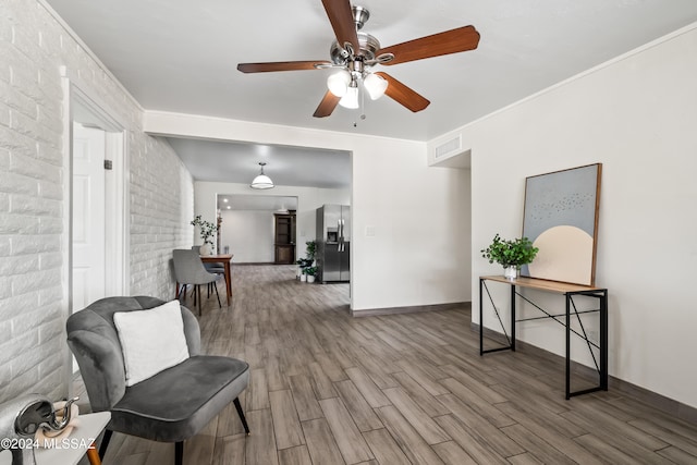 sitting room with crown molding, hardwood / wood-style flooring, brick wall, and ceiling fan