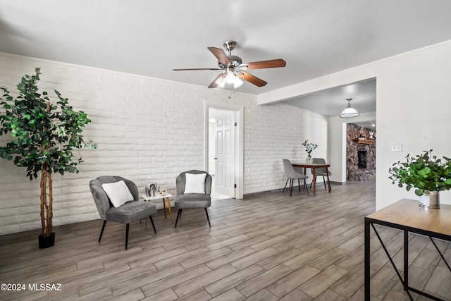 living area with ceiling fan, brick wall, light wood-type flooring, and a stone fireplace