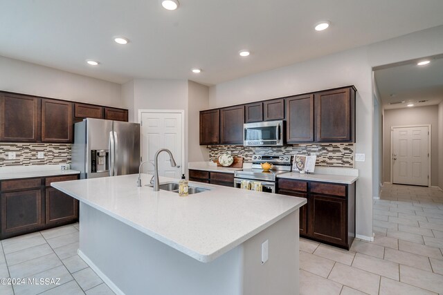 kitchen featuring appliances with stainless steel finishes, sink, dark brown cabinets, decorative backsplash, and a center island with sink