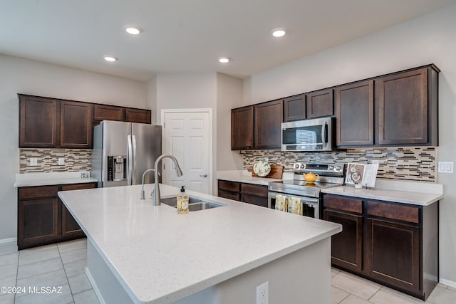 kitchen featuring light tile patterned floors, appliances with stainless steel finishes, sink, an island with sink, and tasteful backsplash