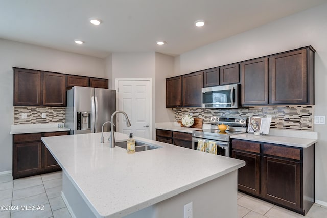 kitchen with light tile patterned floors, a sink, dark brown cabinets, appliances with stainless steel finishes, and an island with sink