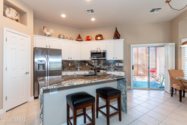 kitchen with a kitchen island with sink, appliances with stainless steel finishes, a kitchen bar, and white cabinets