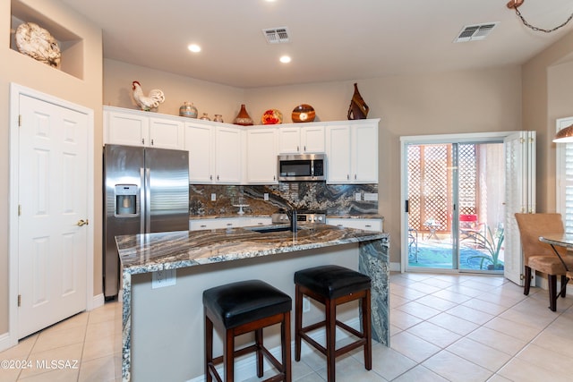 kitchen featuring stainless steel appliances, visible vents, decorative backsplash, and dark stone counters