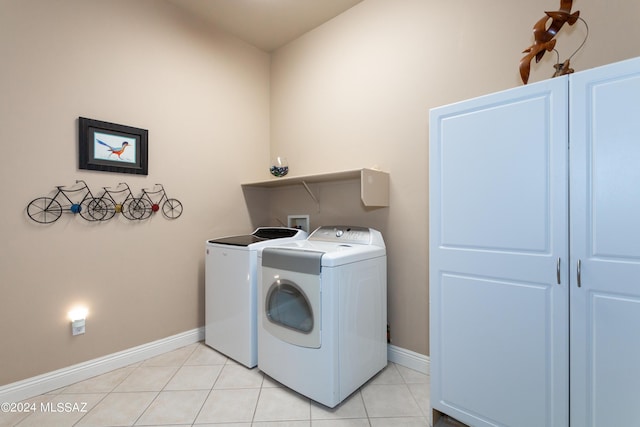 clothes washing area featuring light tile patterned floors, laundry area, independent washer and dryer, and baseboards