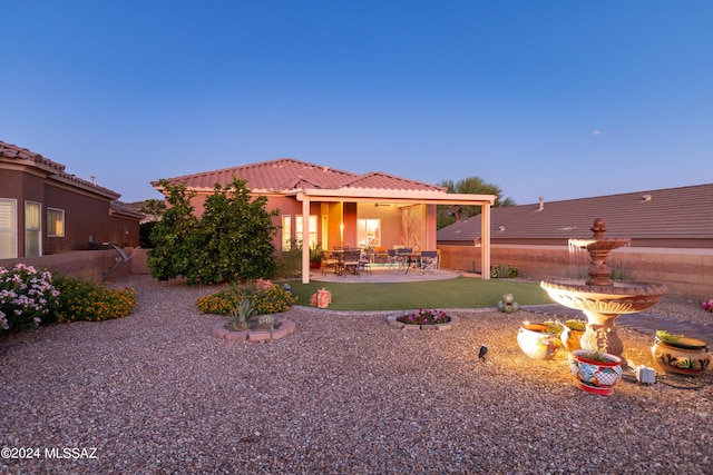 back of house at dusk with stucco siding, a lawn, a patio, fence, and a tiled roof