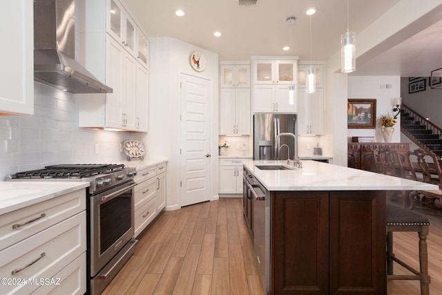 kitchen with light wood-type flooring, light stone counters, wall chimney exhaust hood, stainless steel appliances, and decorative light fixtures