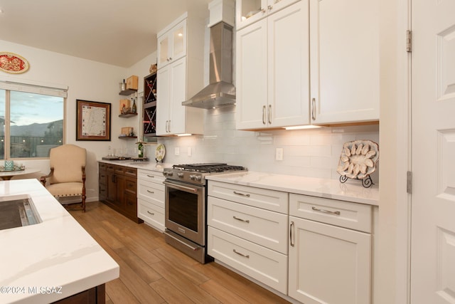 kitchen featuring wall chimney range hood, tasteful backsplash, light hardwood / wood-style flooring, high end stove, and white cabinets