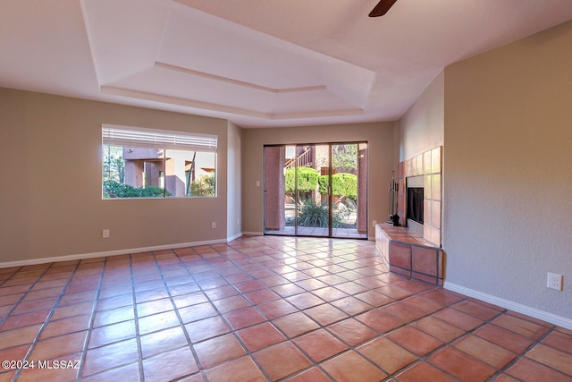 unfurnished living room with ceiling fan, light tile patterned flooring, a raised ceiling, and a tile fireplace