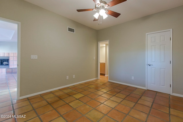 tiled spare room featuring ceiling fan and a tiled fireplace