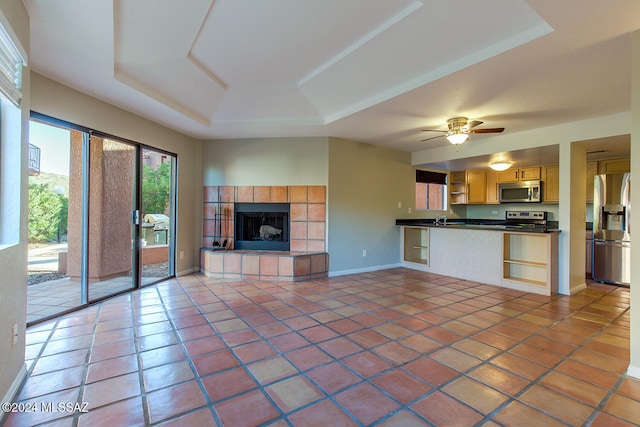 unfurnished living room featuring a fireplace, a tray ceiling, ceiling fan, sink, and tile patterned flooring