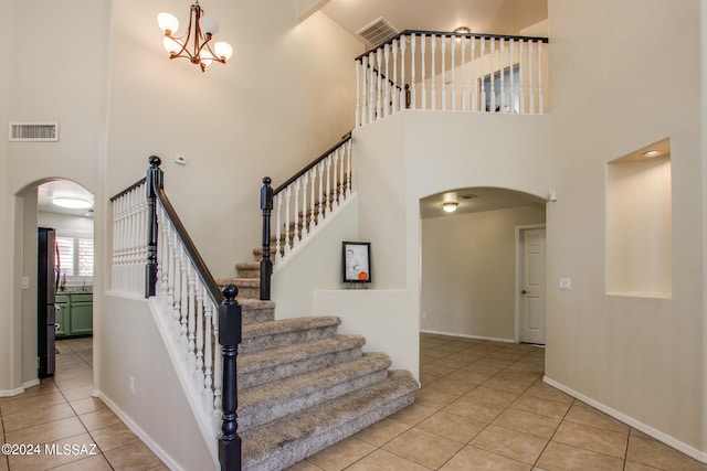 stairs with tile patterned flooring, a high ceiling, and a notable chandelier