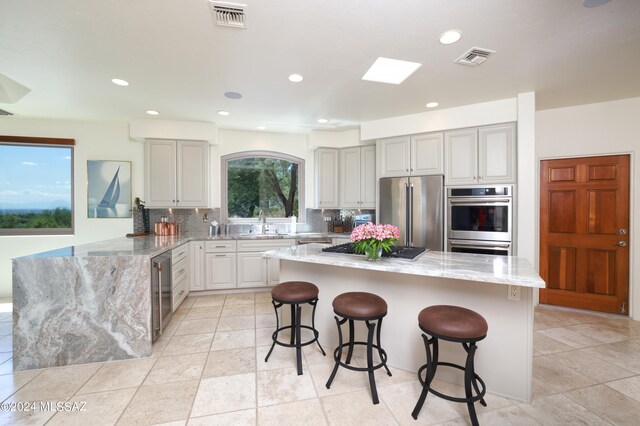 kitchen featuring a kitchen bar, tasteful backsplash, appliances with stainless steel finishes, kitchen peninsula, and light stone countertops