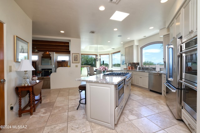 kitchen with a kitchen island, white cabinetry, a breakfast bar area, light stone counters, and stainless steel appliances