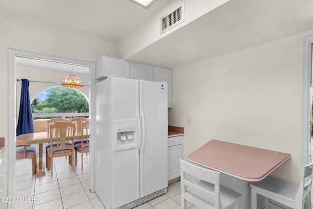 kitchen with an inviting chandelier, light tile patterned floors, hanging light fixtures, white cabinetry, and white fridge with ice dispenser