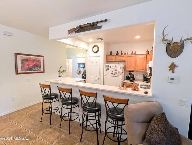 kitchen featuring a kitchen bar, kitchen peninsula, white appliances, and light tile patterned flooring