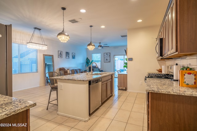 kitchen featuring stainless steel appliances, a kitchen breakfast bar, ceiling fan, pendant lighting, and a kitchen island with sink