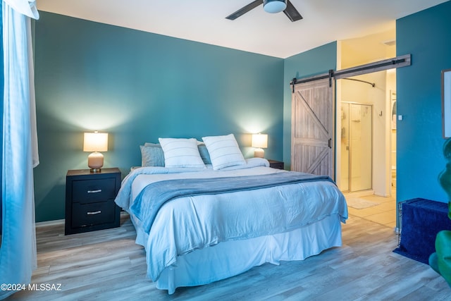 bedroom featuring a ceiling fan, a barn door, wood finished floors, and ensuite bathroom