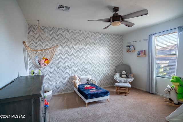carpeted bedroom featuring an accent wall, baseboards, visible vents, and a ceiling fan