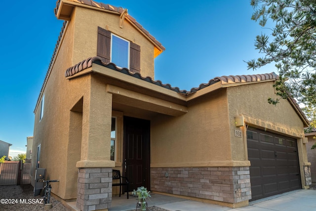 mediterranean / spanish house with stucco siding, stone siding, an attached garage, and a tiled roof