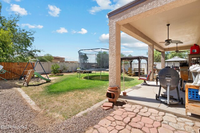 view of yard featuring ceiling fan, a patio area, a trampoline, and a playground