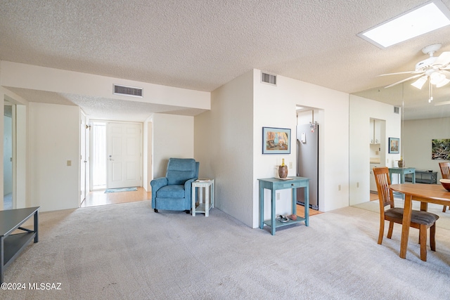 sitting room featuring a skylight, ceiling fan, carpet, and a textured ceiling