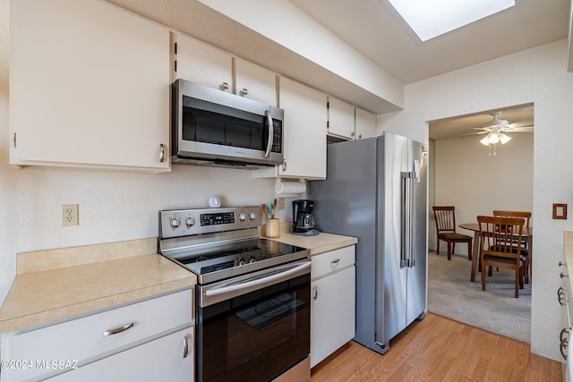 kitchen featuring a skylight, stainless steel appliances, light hardwood / wood-style floors, white cabinetry, and ceiling fan