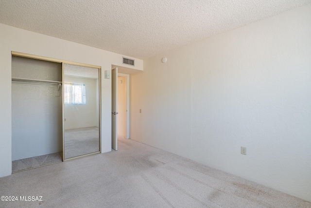 unfurnished bedroom with light carpet, a textured ceiling, and a closet