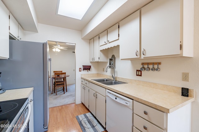 kitchen with a skylight, dishwasher, sink, ceiling fan, and white cabinets