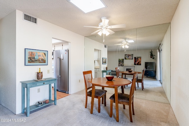 dining space with light colored carpet, a skylight, ceiling fan, and a textured ceiling