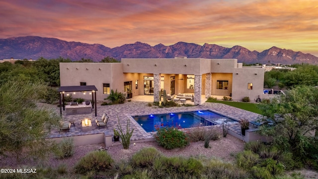 back of property at dusk with a mountain view, an outdoor living space with a fire pit, and stucco siding