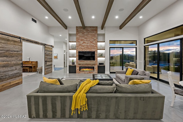 living room with a barn door, a high ceiling, a brick fireplace, and beam ceiling